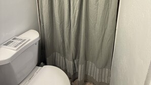 A bathroom with a white toilet, a beige shower curtain, and a white wall. - Cozy Studio 2@Casa Marvella / Water Tank (San Juan)