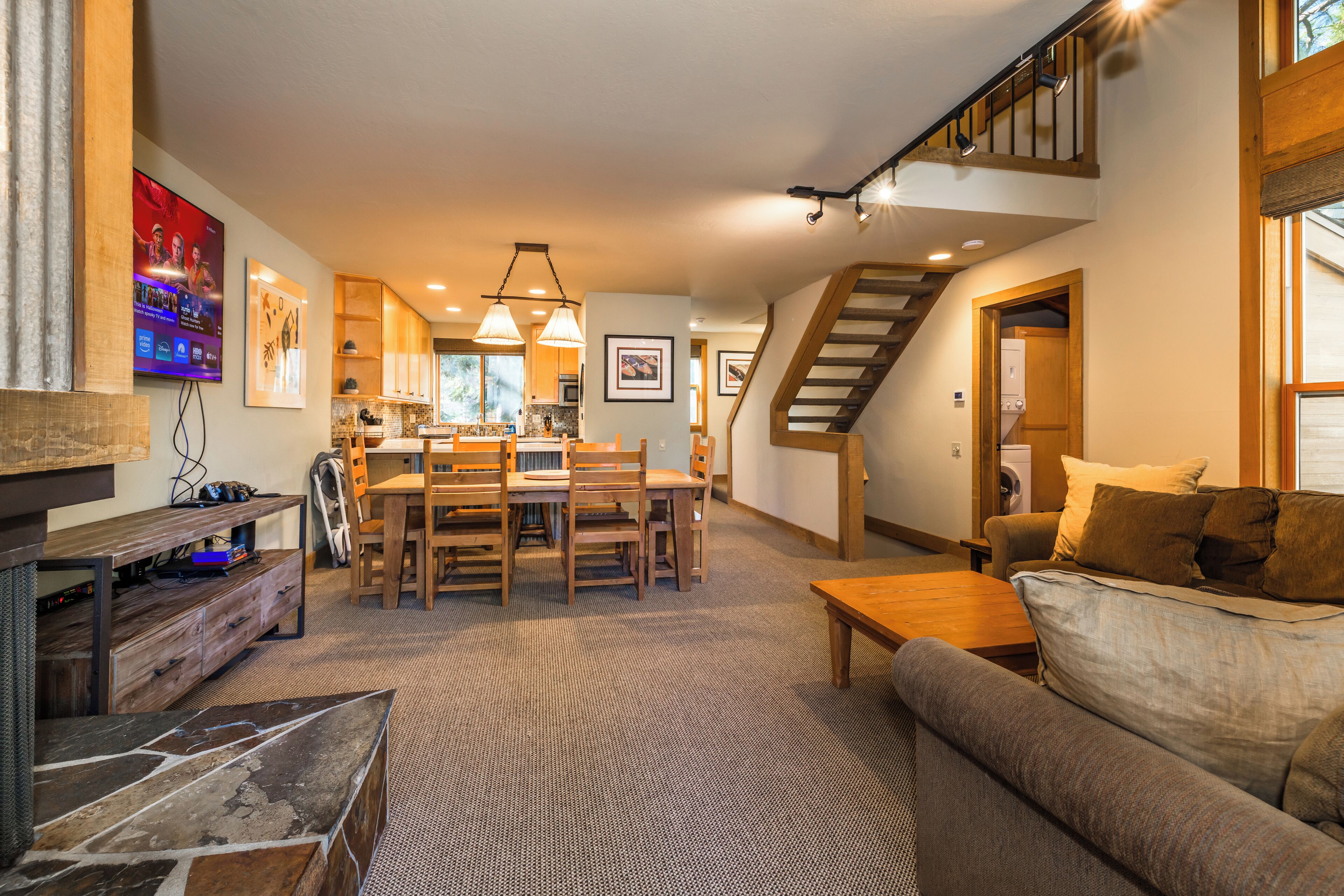 A spacious living area with a dining table, wooden chairs, a sofa, and a staircase leading to an upper level.