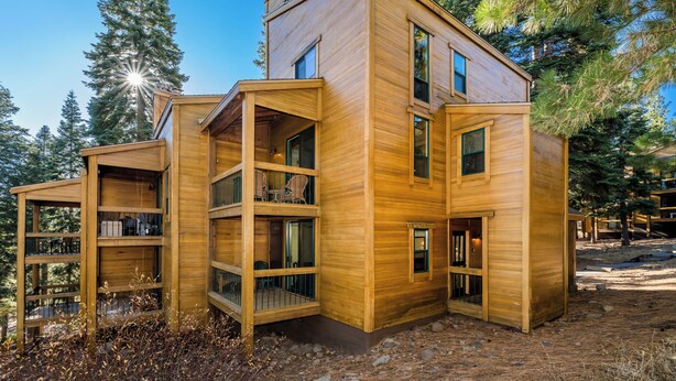 Eine moderne Holz-Blockhütte mit mehreren Balkonen und großen Fenstern, umgeben von Bäumen.