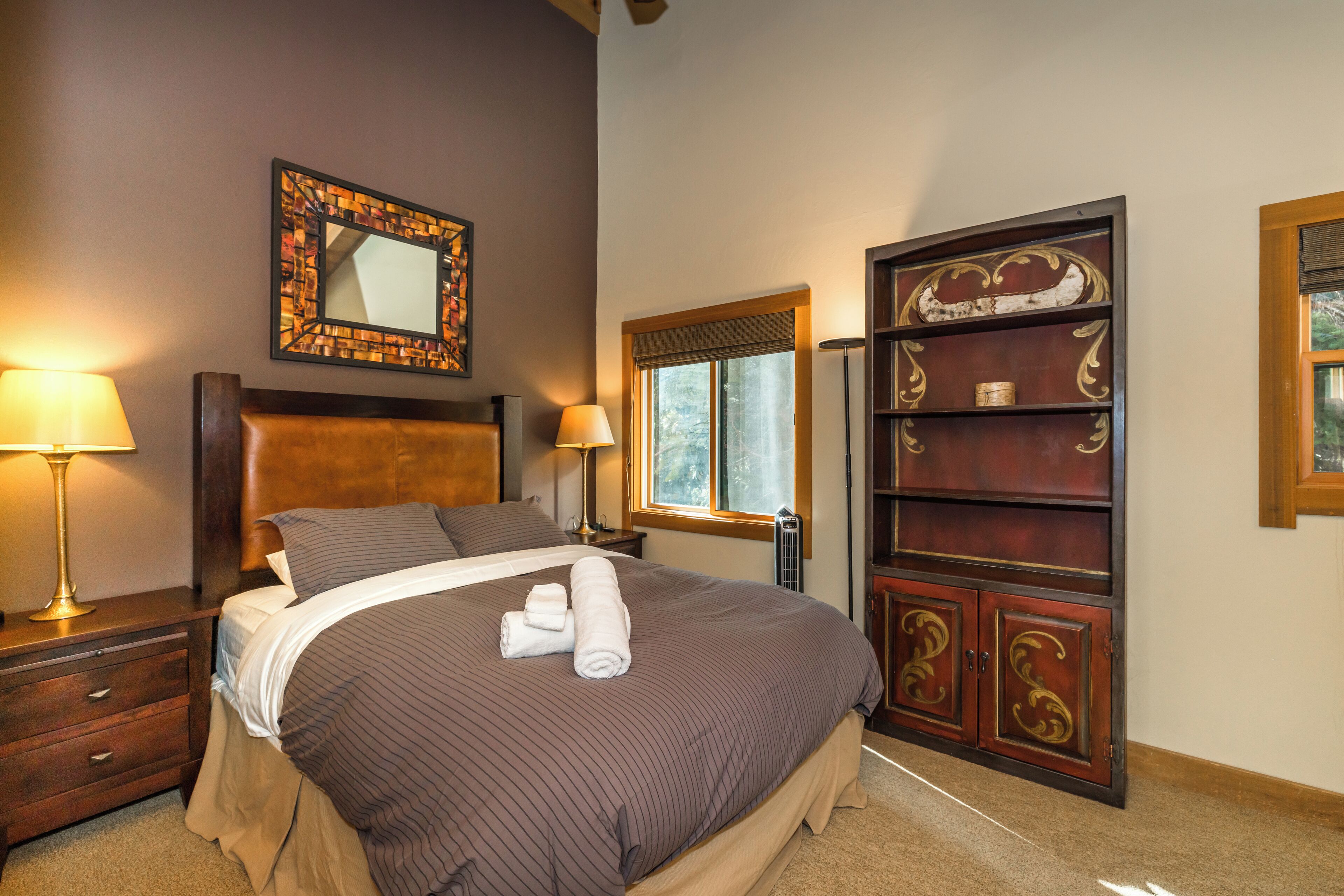 Una cama bien hecha con cabecera, dos lámparas de noche, una ventana con vistas y un mueble de madera decorativo.