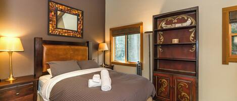 Una cama bien hecha con cabecera, dos lámparas de noche, una ventana con vistas y un mueble de madera decorativo.
