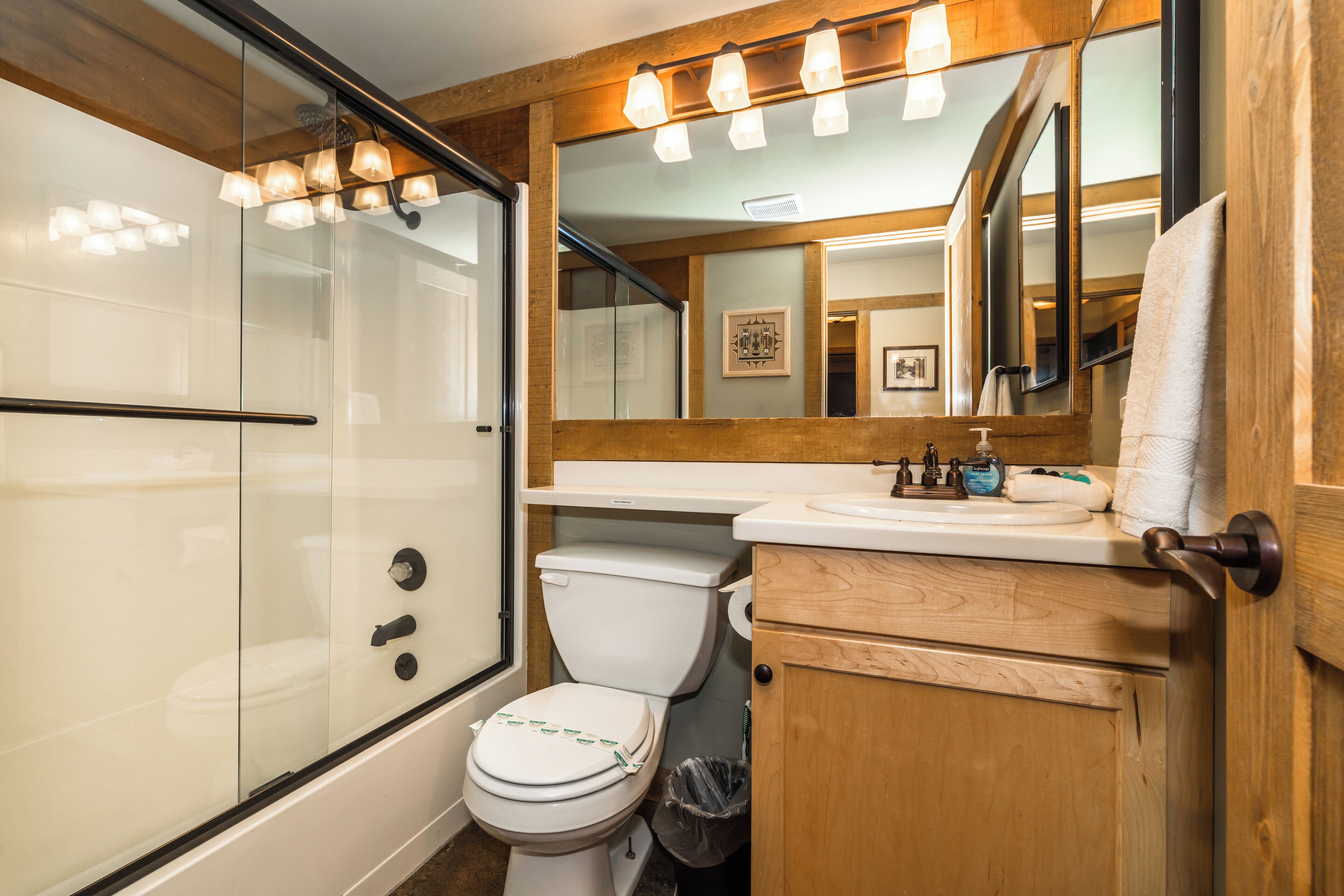 A bathroom with a glass-enclosed shower, a white toilet, a wooden vanity with a mirror, and a sink with a faucet.