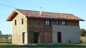 A modern wooden house with a stone extension, large windows, and a sloped roof.