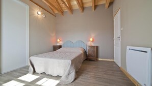 A bedroom with a bed, two bedside tables with lamps, a radiator, and a wooden ceiling.