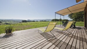 A wooden deck with two yellow chairs and a table, overlooking a green field and distant hills.