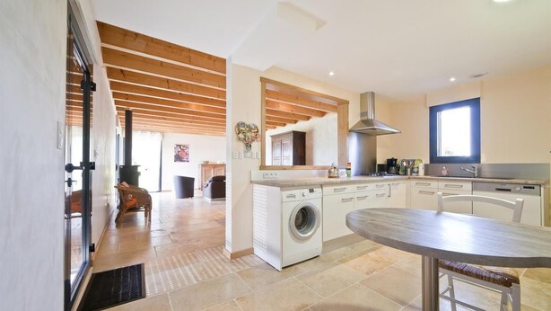 A modern kitchen with a built-in washing machine, a dining area with a round table, and a view of the living room.
