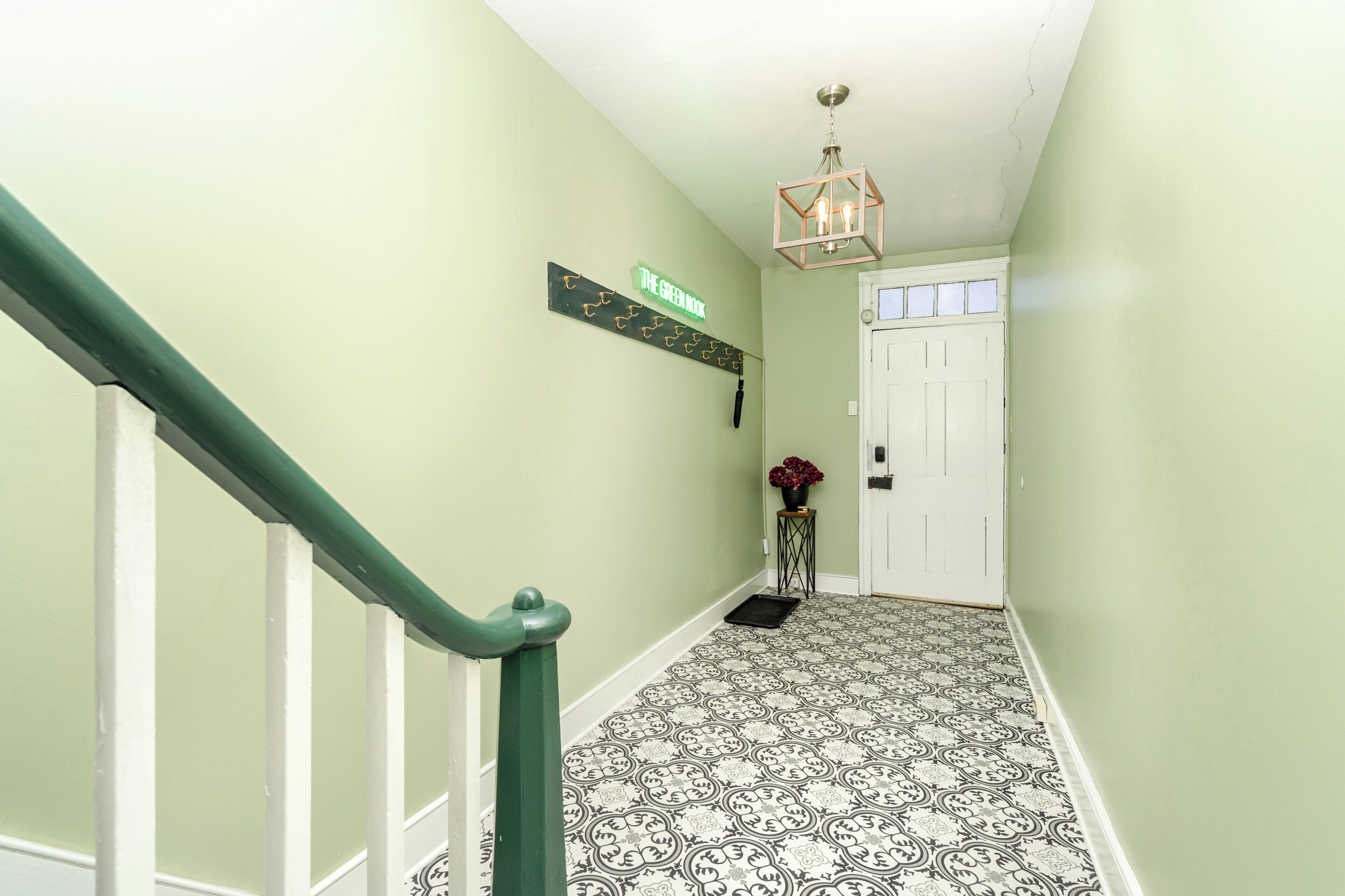 A hallway with a green wall, a white door, a patterned floor, and a green railing.