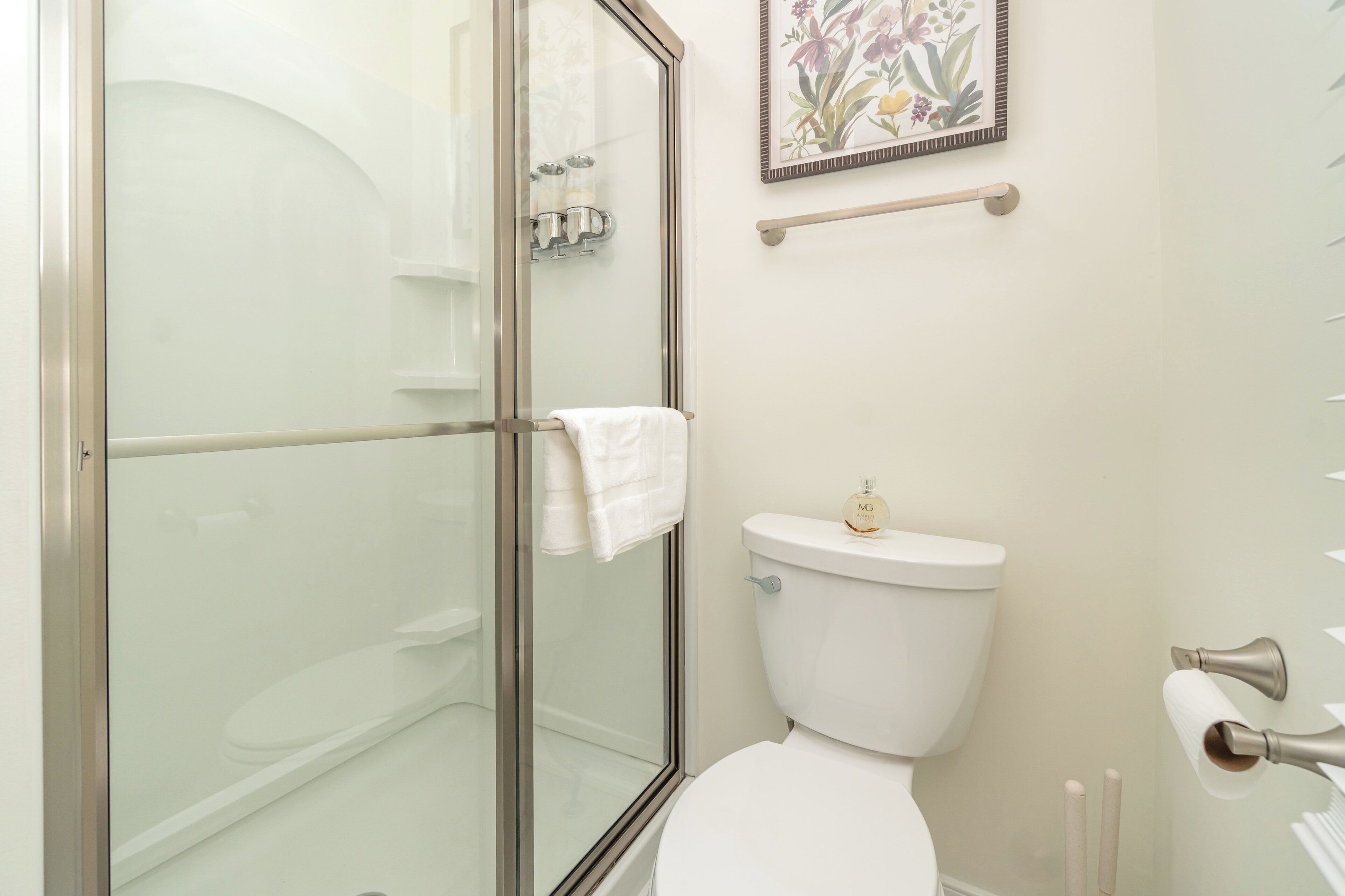 Une salle de bain avec une douche à parois de verre, des toilettes et une œuvre d’art florale encadrée au mur.