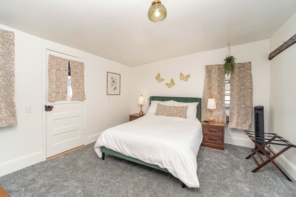 A bedroom with a bed, bedside tables, a heater, and patterned curtains.