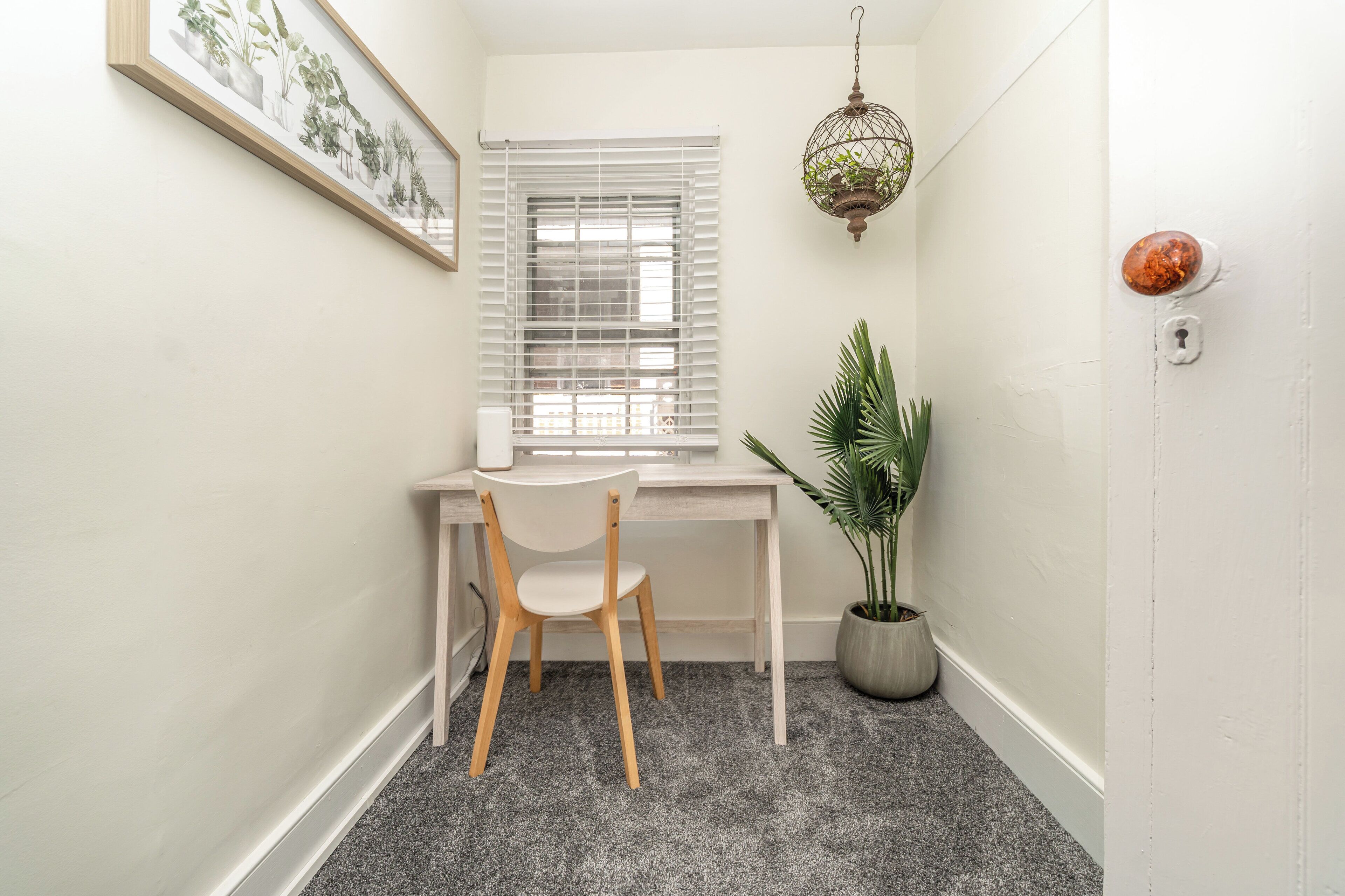 Une petite pièce, bien rangée, avec un bureau, une chaise, une plante en pot et une fenêtre équipée de stores.