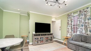 En stue med et fladskærms-tv, en grå sofa og et spisebord med stole.