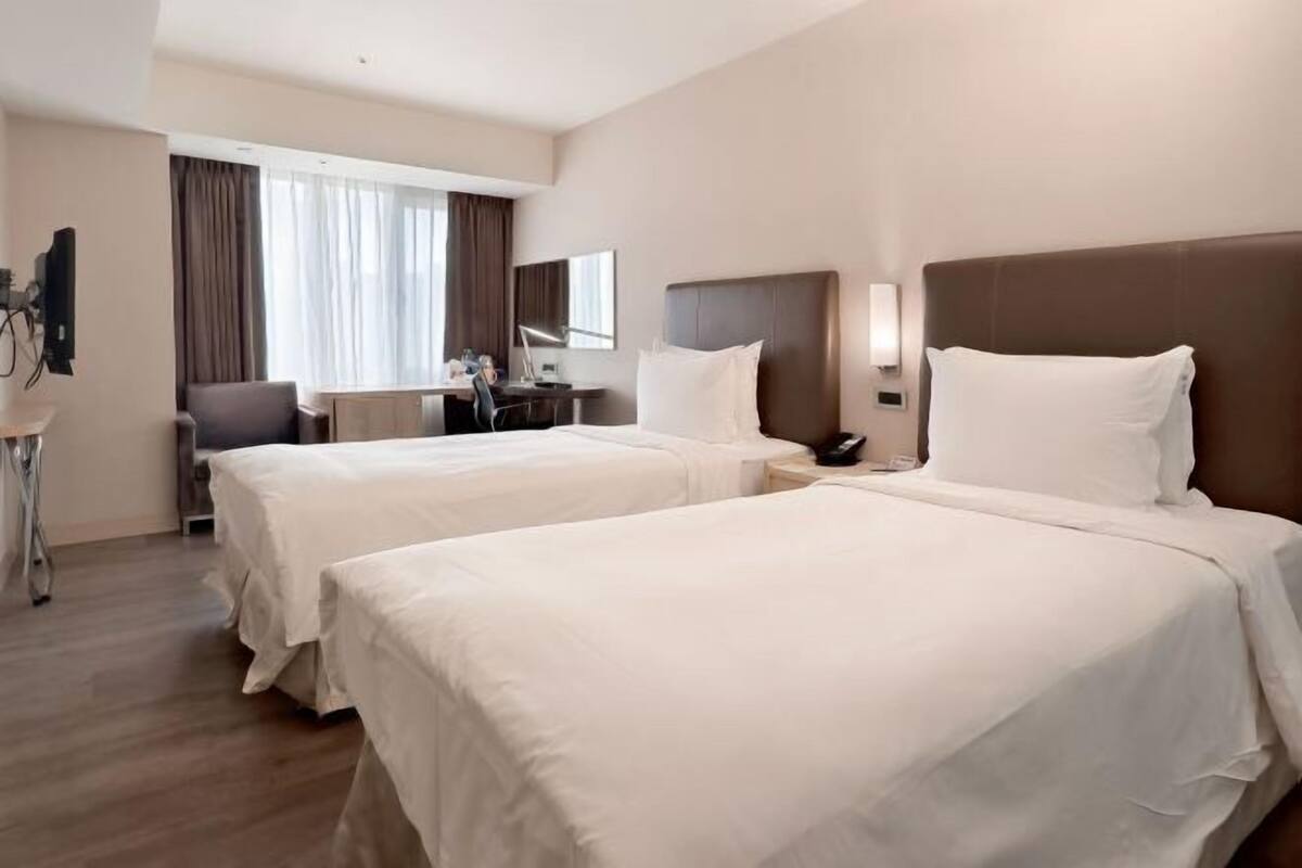 A hotel room with two beds, a desk, a chair, and a TV.