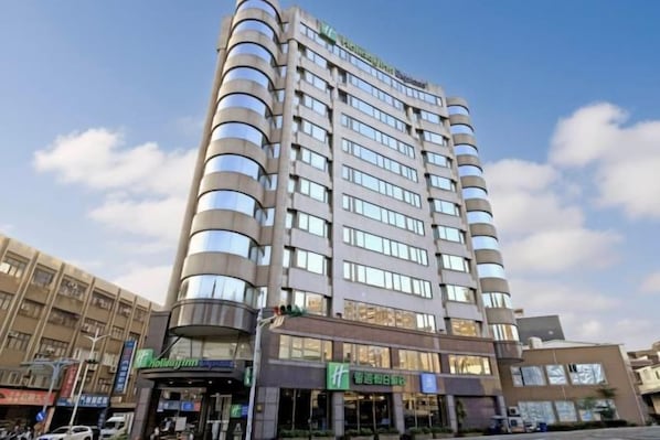 Un hotel de varios pisos con diseño moderno, que cuenta con balcones en cada planta y una entrada destacada con señalización.