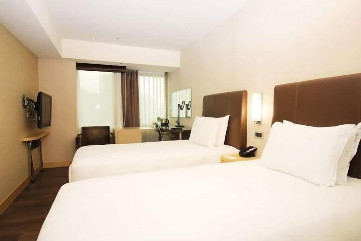 A hotel room with two beds, a desk, a chair, a TV, and a window with curtains.
