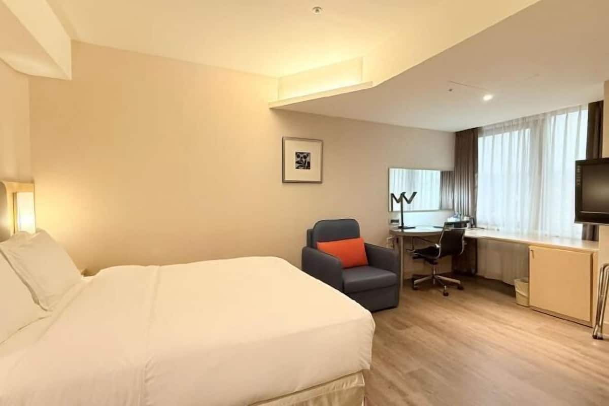 A hotel room with a bed, desk, chair, TV, and a framed picture on the wall.