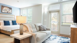 A modern bedroom with a bed, a sofa, a lamp, and a TV. - Landing Furnished Apartments South End Stratford (Stratford)