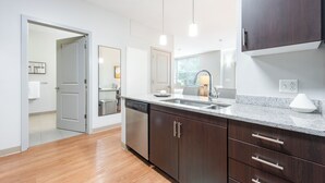 A modern kitchen with dark wooden cabinets, a granite countertop, and pendant lighting. - Landing Furnished Apartments South End Stratford (Stratford)