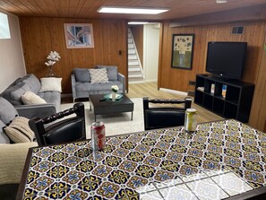 A living room with a grey sofa, a coffee table, a patterned tablecloth, and a television on a wooden cabinet. - 12 Min to Great Lakes Naval Station Navy Graduation Family Home (Waukegan)