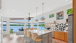 A modern kitchen with a large island, bar stools, and a view of the water. - New! Modern lakeside retreat-hot tub-trails-kayak (La Porte)