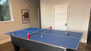 A table tennis table with a blue playing surface and net, positioned in a room with a white door and a poster on the wall. - New! Modern lakeside retreat-hot tub-trails-kayak (La Porte)