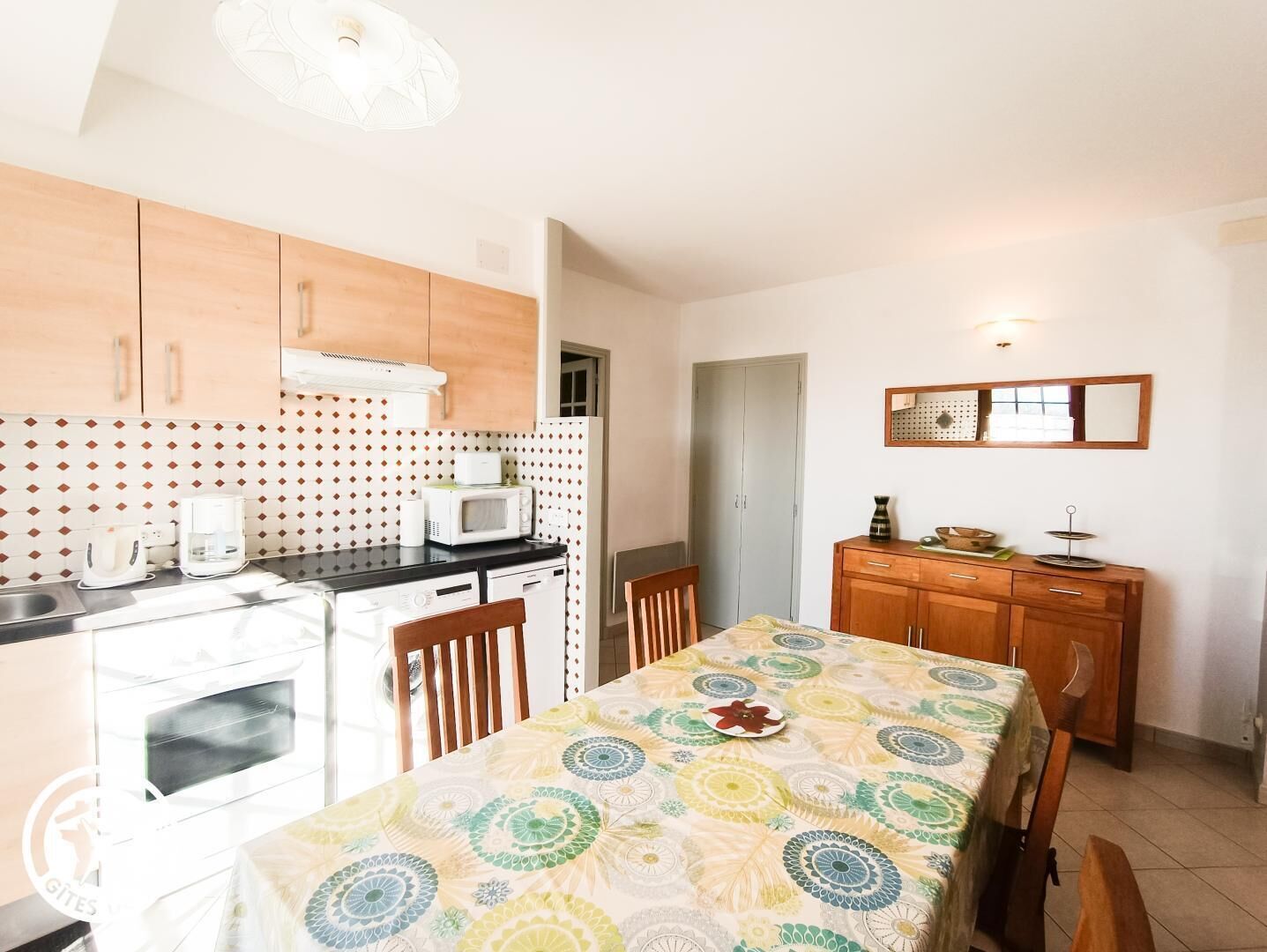 Eine kompakte Küche mit Mikrowelle, Toaster und Backofen. Ein Esstisch mit Stühlen und ein Holzschrank mit Spiegel darüber.