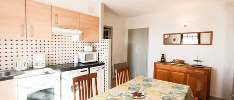 Eine kompakte Küche mit Mikrowelle, Toaster und Backofen. Ein Esstisch mit Stühlen und ein Holzschrank mit Spiegel darüber.