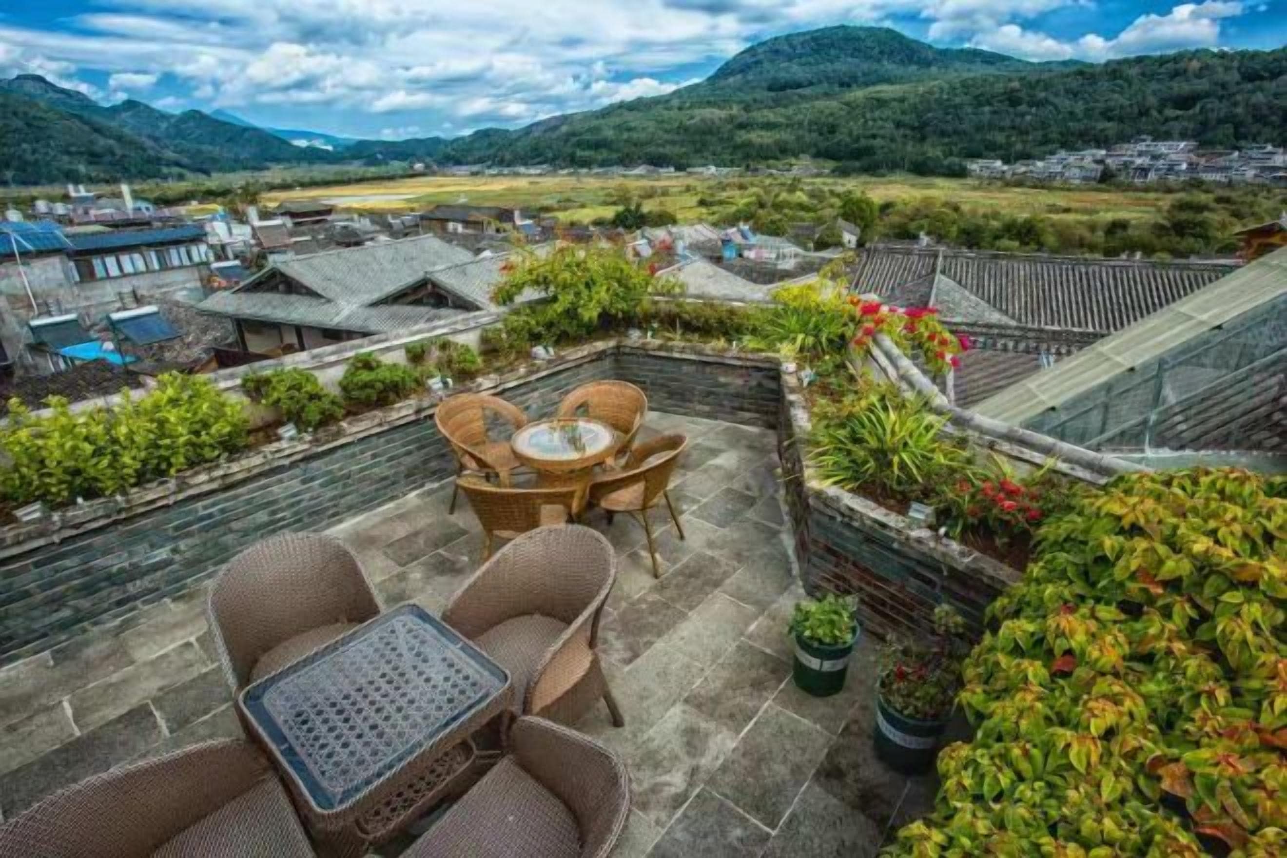 Una terraza en la azotea con mobiliario de mimbre, plantas en macetas y vistas a un pueblo tradicional.