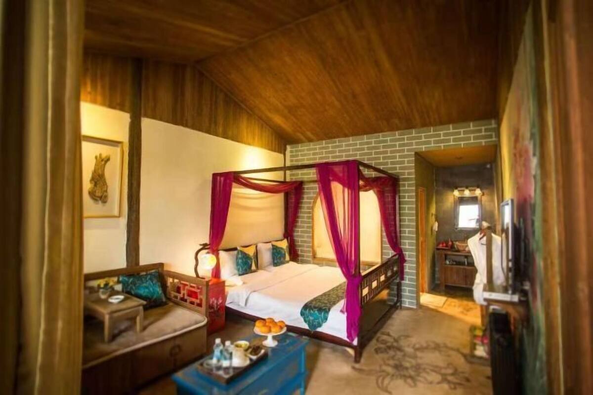 A room with a four-poster bed, a sofa, a small table with a tray of fruit, and a television.