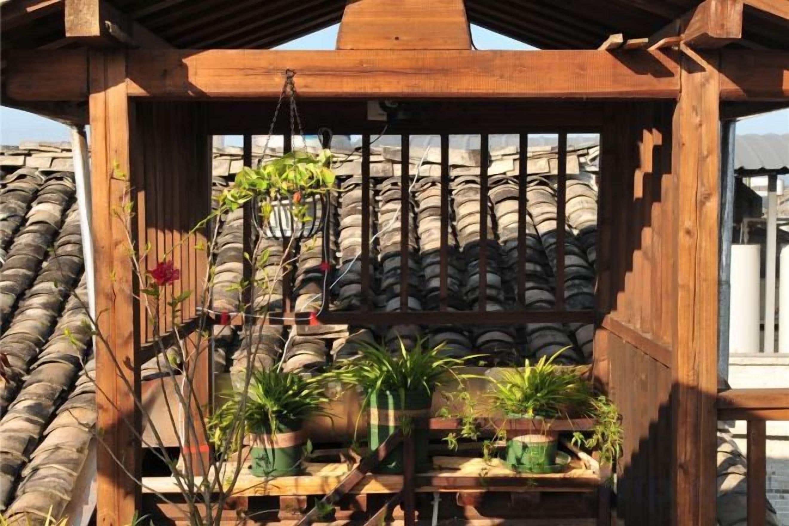 A wooden pergola with potted plants and a view of a tiled roof.