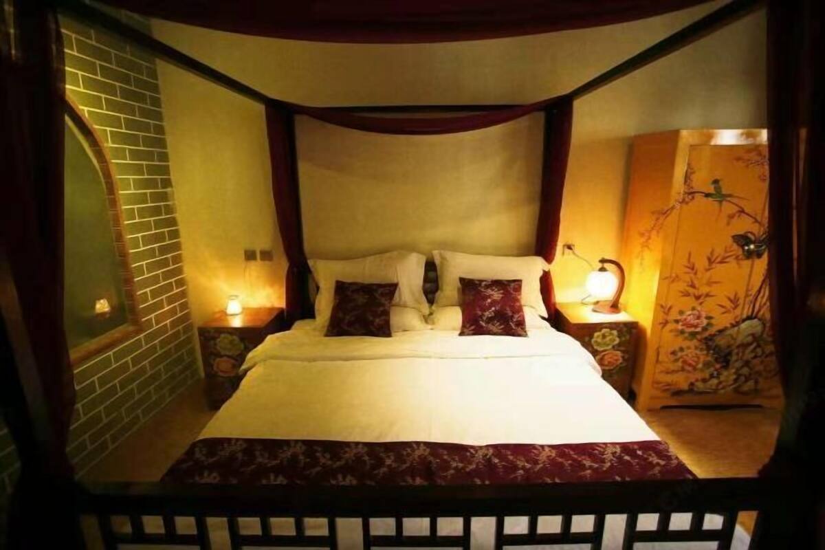 A bedroom with a four-poster bed, a brick wall, and a nightstand with a lamp.