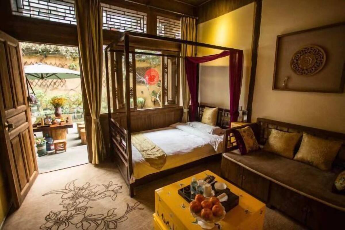 A traditional room with a four-poster bed, a sofa, and a small table with a tray of fruit.