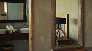 A bedroom with a bed, a wooden nightstand, a mirror, and a bathroom visible through an open door. - Cocaloba Adobe by Wynwood House (Máncora)