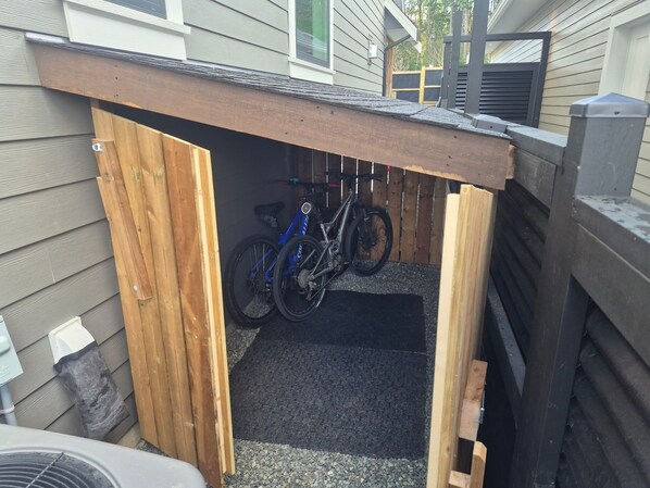 A wooden bike shed with a roof, a gravel floor, and a bicycle inside. - Brand New Suite Close to Mt. Washington, Cumberland Bike Trails and the Ocean. (Royston)