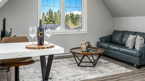 Een moderne woonkamer met een eettafel, een bank en uitzicht op bomen door een groot raam.