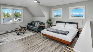 Een slaapkamer met een groot bed, een grijze bank, een klein bijzettafeltje en een plafondventilator.