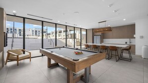 A modern pool table in a bright room with large windows, a sofa, and a bar area. - Sleep 6 in Resort Style Community- Near Stadium (North Miami)