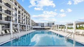 A swimming pool with lounge chairs and a multi-story building in the background. - Sleep 6 in Resort Style Community- Near Stadium (North Miami)