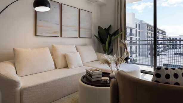 A modern living room with a sofa, a coffee table with books, and a view of a cityscape through large windows. - Sleep 6 in Resort Style Community- Near Stadium (North Miami)