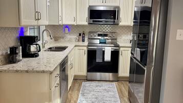 A modern kitchen with white cabinetry, stainless steel appliances, and a patterned rug.