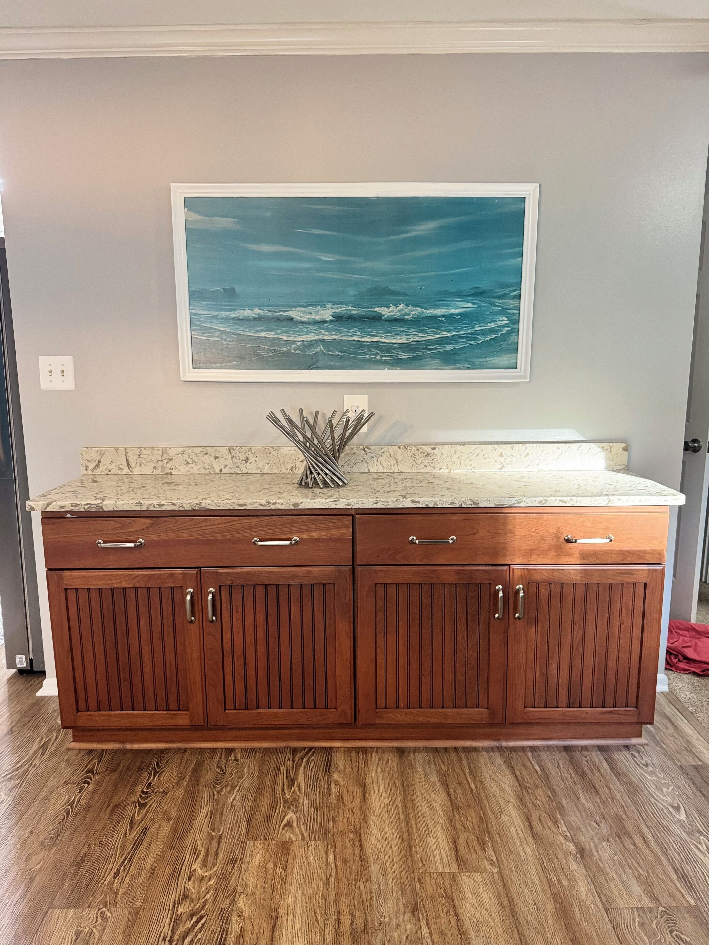 A wooden kitchen island with a marble countertop and a framed ocean painting above it.