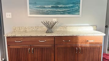 A wooden kitchen island with a marble countertop and a framed ocean painting above it.