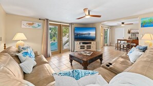 Ett vardagsrum med en tv, lädersoffor, ett soffbord och en matplats med utsikt över havet.