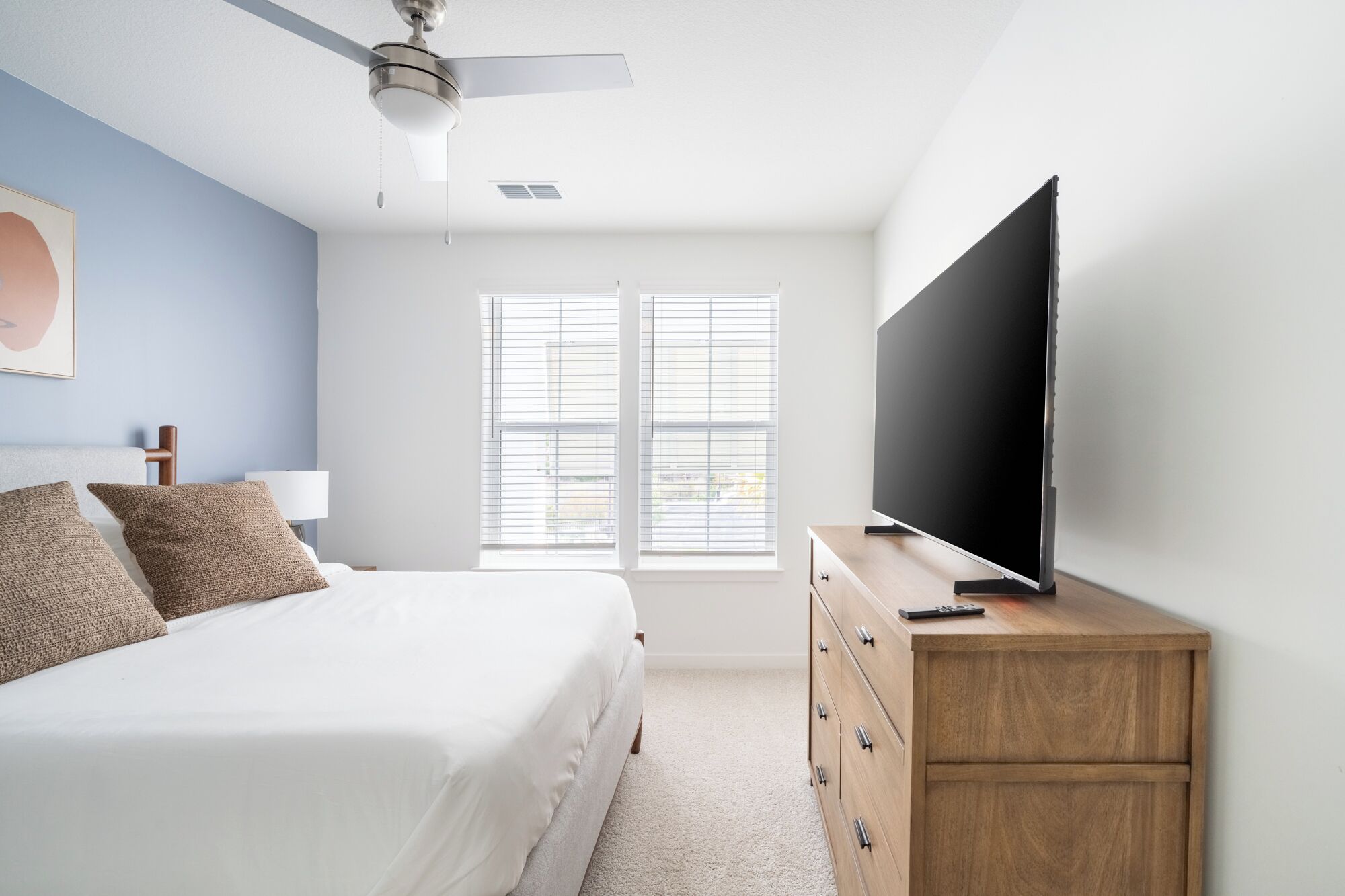 Un dormitorio con cama, cómoda de madera, televisor de pantalla plana y ventilador de techo.