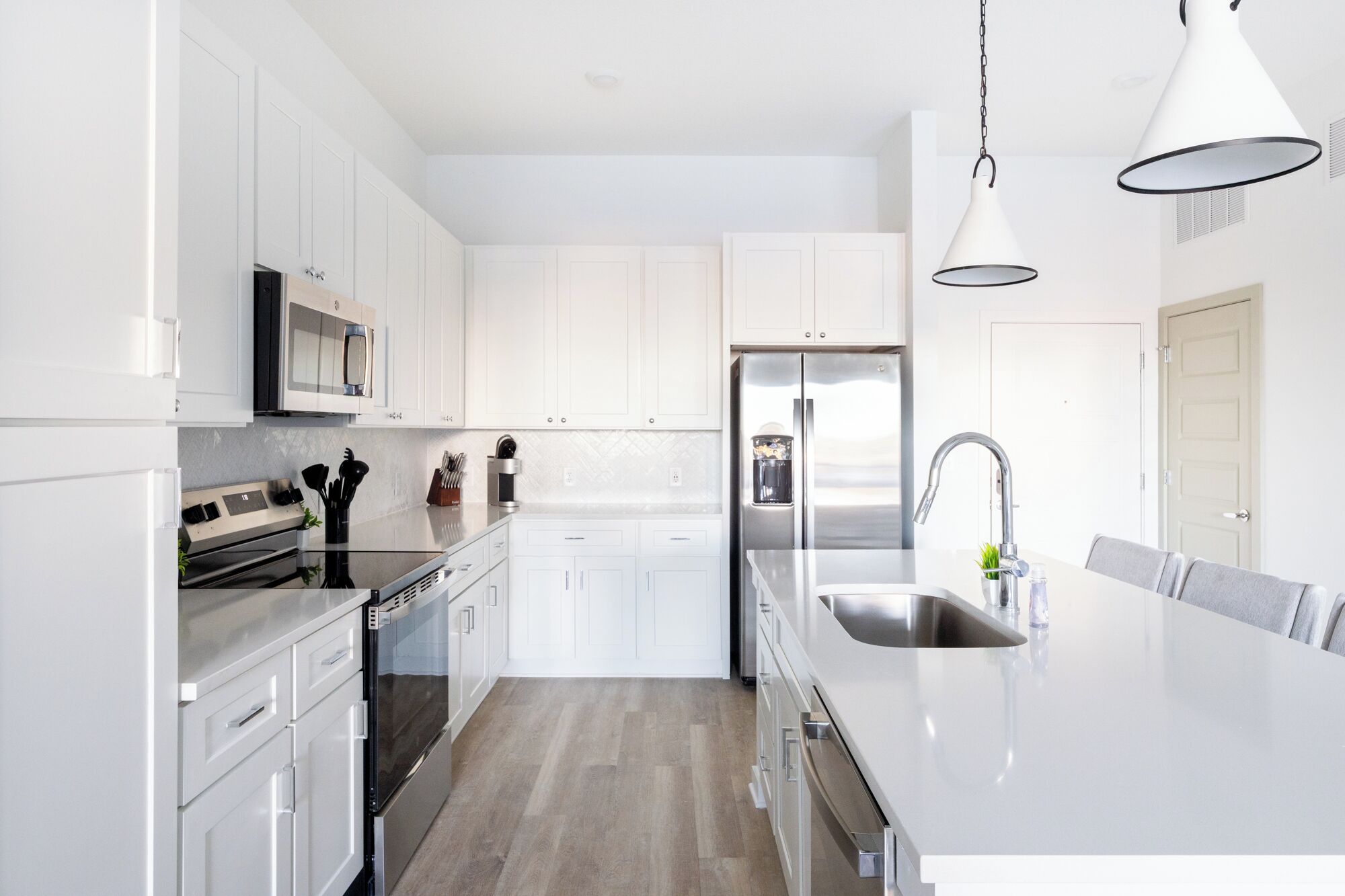 Una cocina moderna con armarios blancos, electrodomésticos de acero inoxidable y una isla grande con un lavamanos.