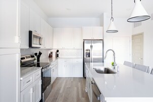 A modern kitchen with white cabinetry, stainless steel appliances, and a large island with a sink.