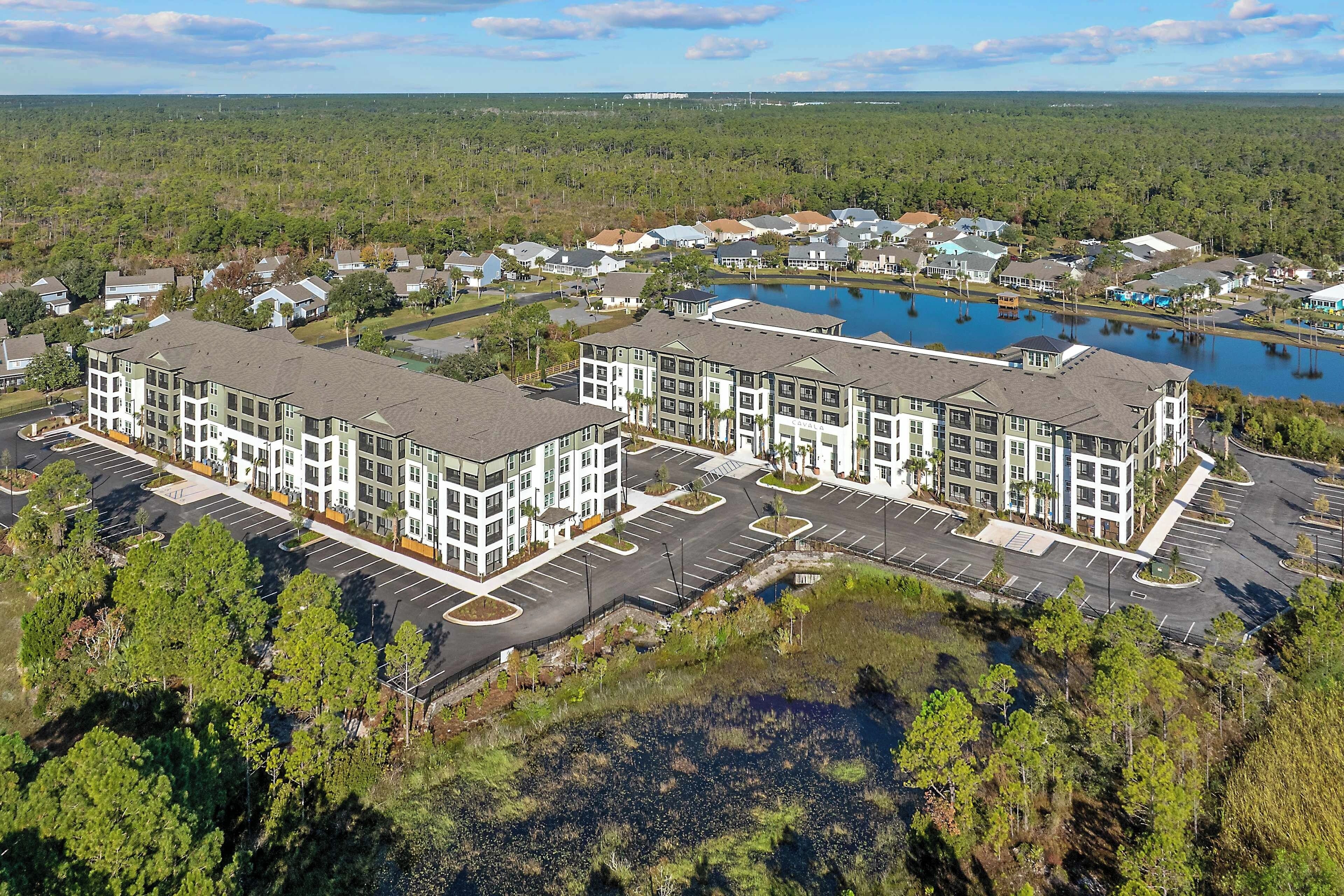 A multi-story residential building with a parking lot and a lake.
