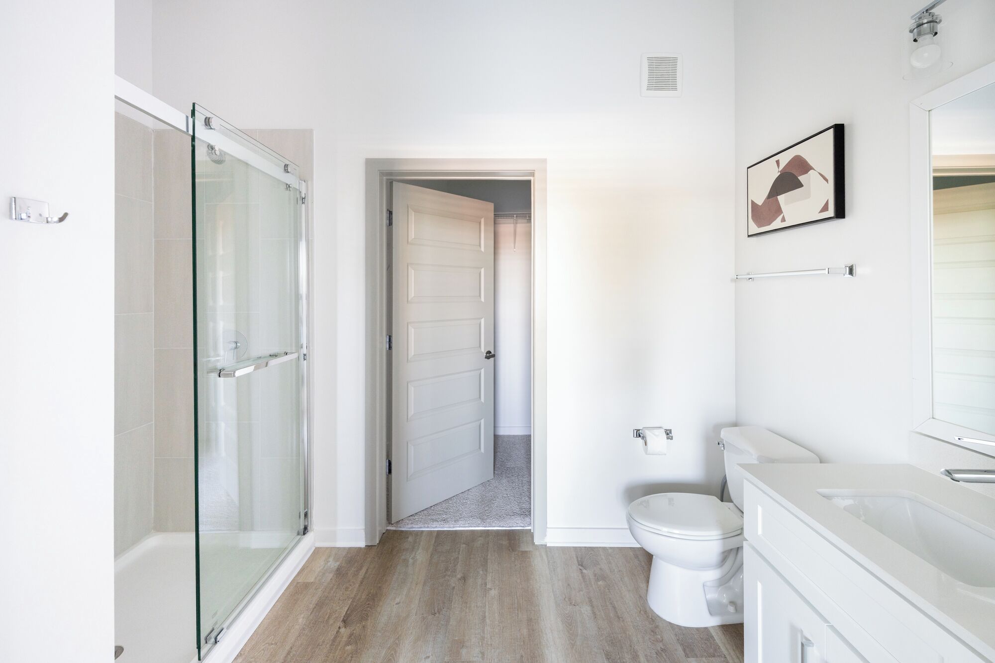 A modern bathroom with a glass shower enclosure, a toilet, and a sink with a mirror.