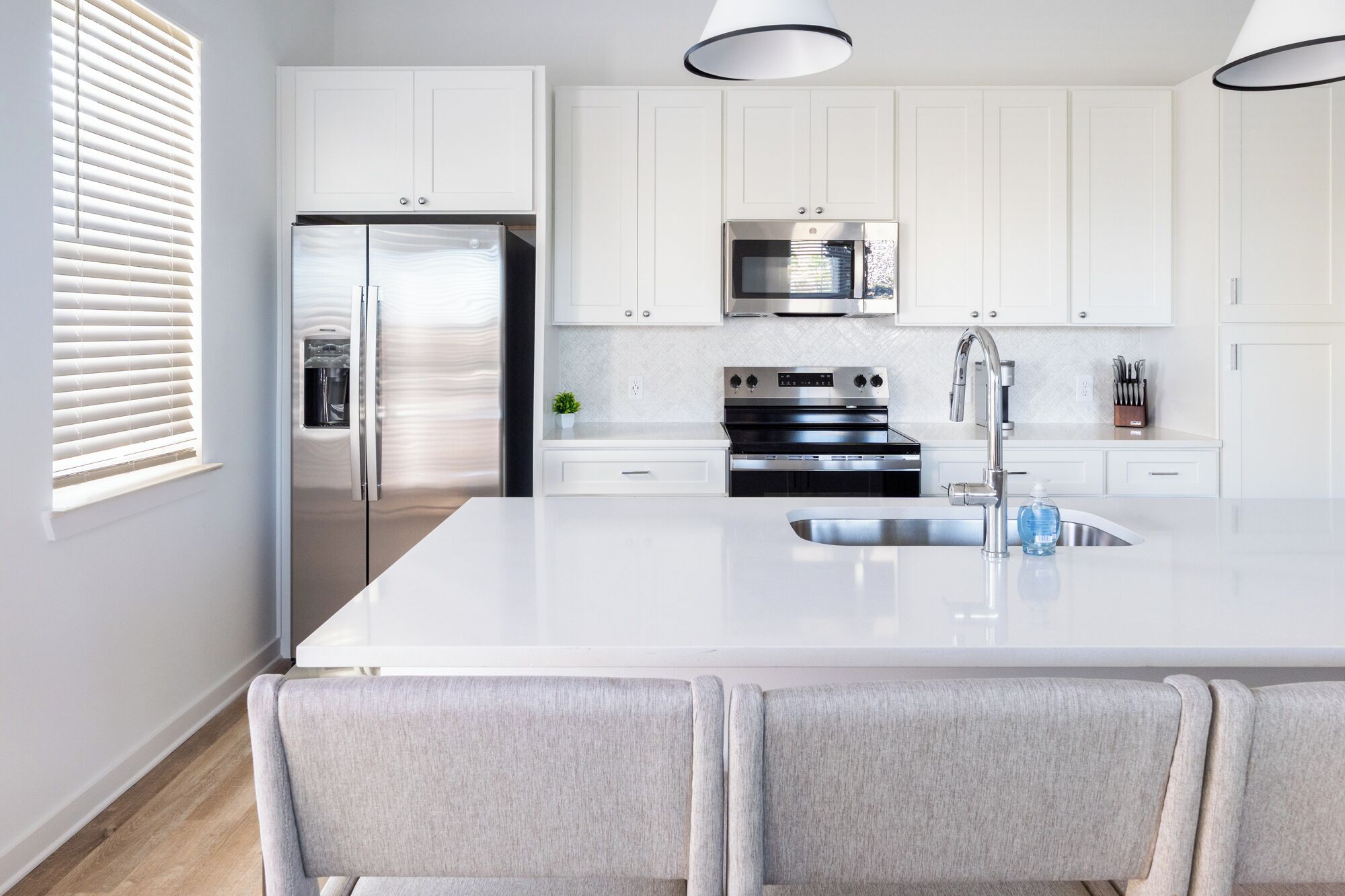 A modern kitchen with white cabinetry, stainless steel appliances, and a central island with bar stools.