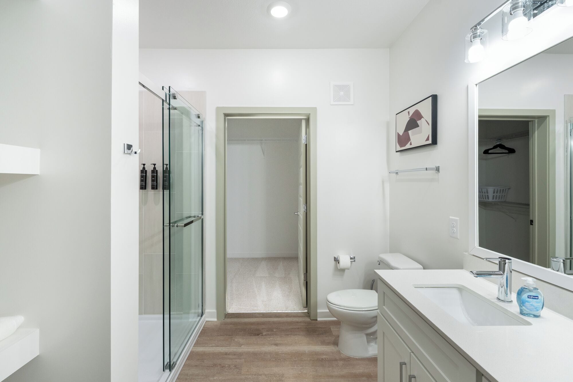 Un baño moderno con cabina de ducha de vidrio, inodoro y lavamanos con un espejo grande.