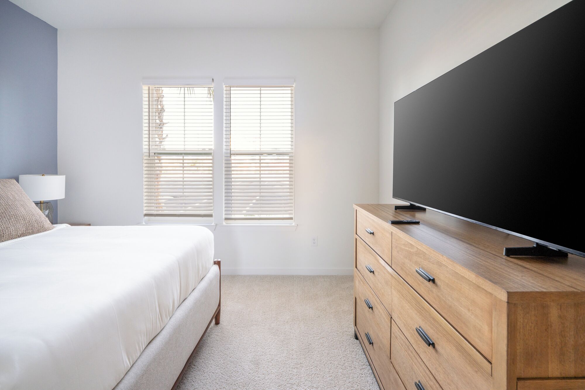 A bedroom with a bed, a dresser, a TV, and a window with blinds.